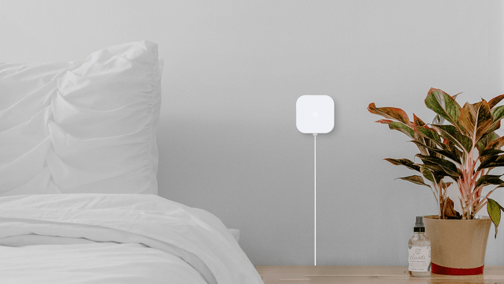 Square white Tellus electronic device mounted on wall next to bed